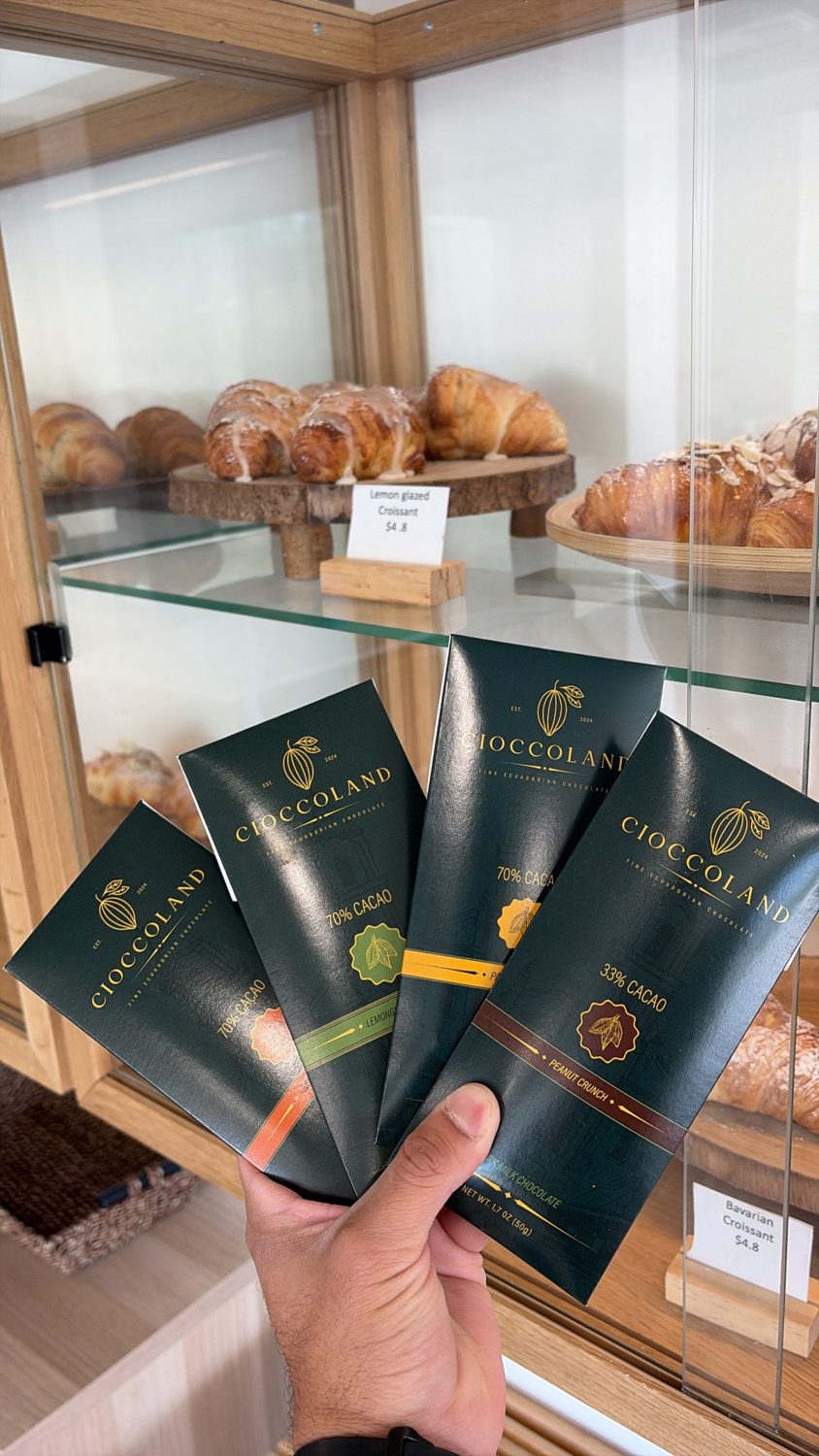 Cioccoland chocolate bars held in hand — 70% cacao and 33% Peanut Crunch, in front of a bakery case