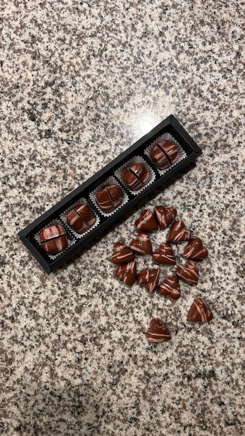 A black gift box of five glossy striped bonbons beside marble-striped heart bonbons